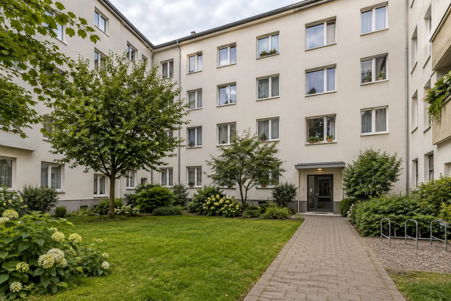 Bewohnt wirkendes Mehrfamilienhaus mit begrüntem Innenhof als neutrales Symbol für den Verkauf einer vermieteten Wohnung
